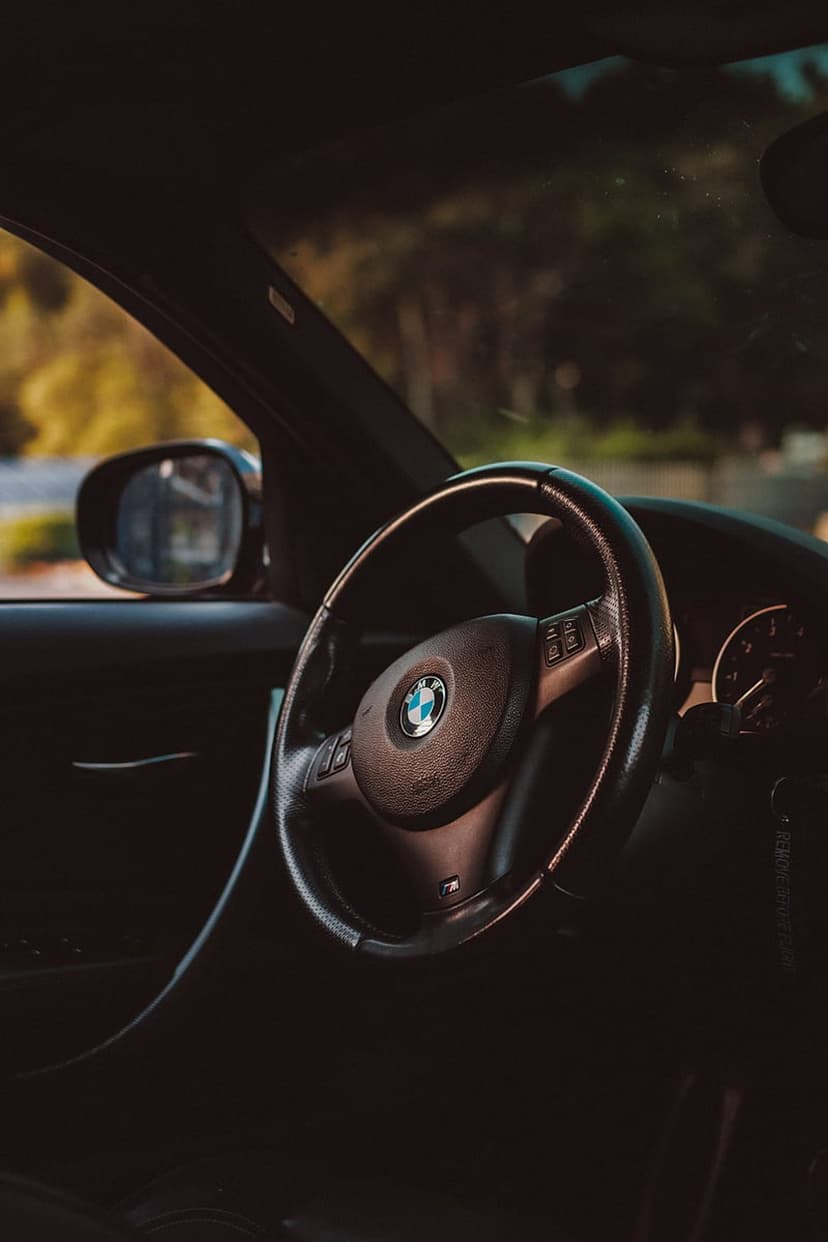 BMW steering wheel with a centered logo and leather texture illuminated by warm golden hour light in a cockpit.