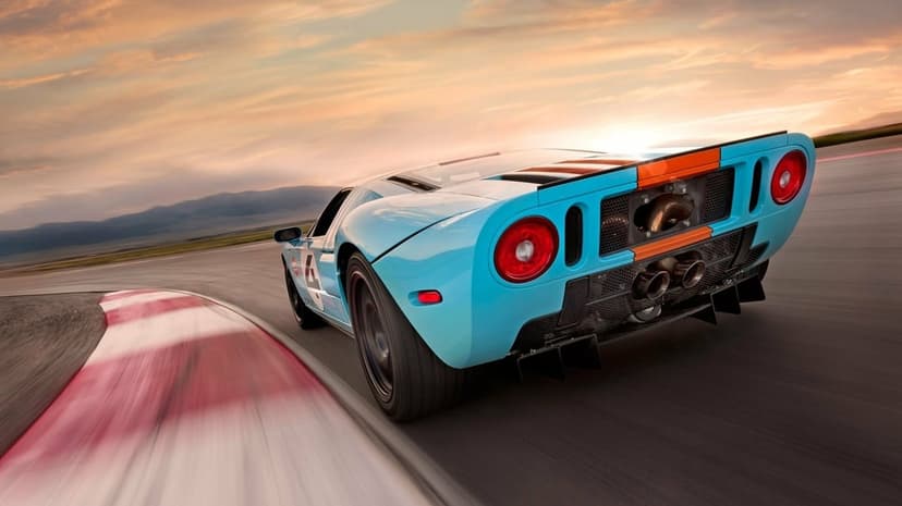 Rear view of a blue and orange Ford GT racing car cornering on a track at sunset with motion blur.
