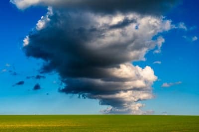 Dramatic Storm Cloud Over Green Field Under Blue Sky