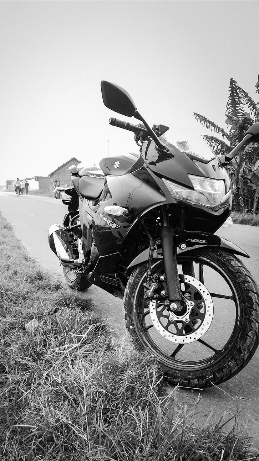 Black Suzuki sport motorcycle parked on a grassy roadside with a distant village building and green trees.