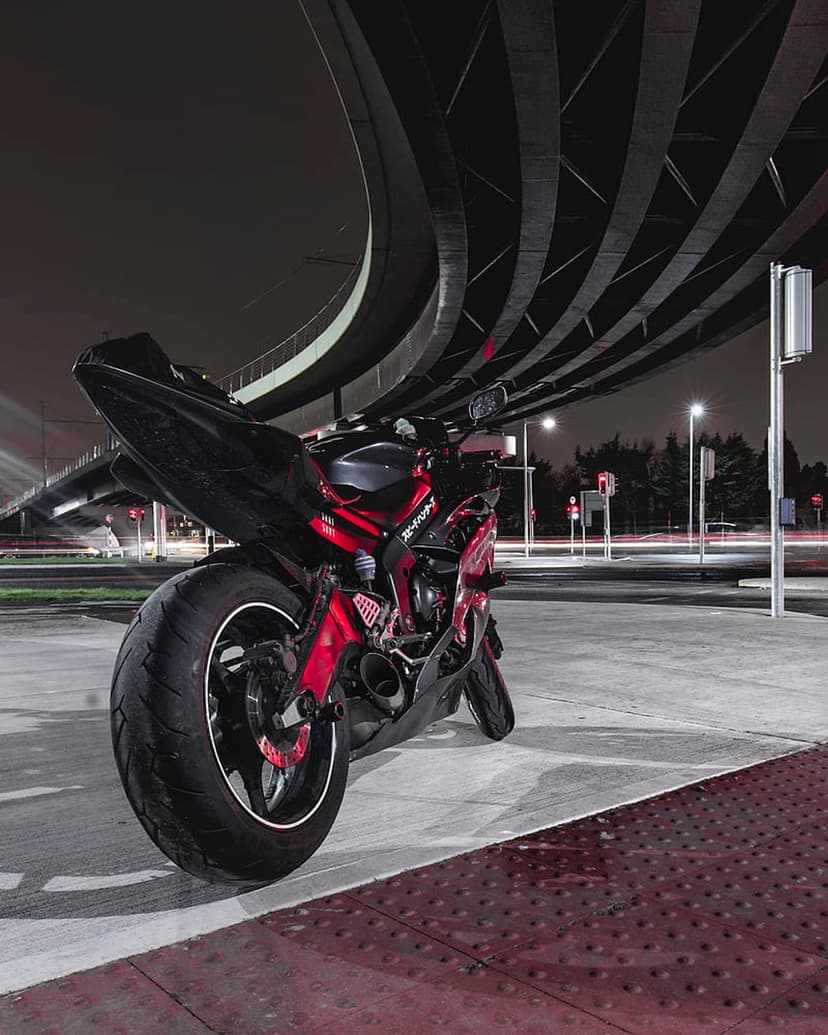 Red and black sport motorcycle parked on concrete under a curved concrete bridge with glowing urban night lights.
