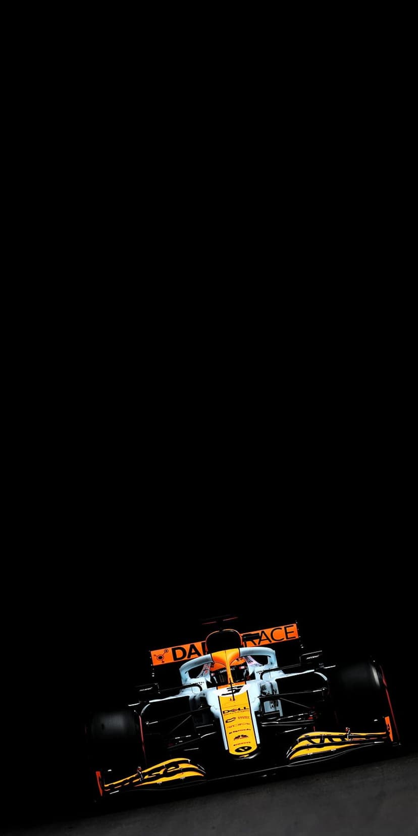 McLaren Formula 1 car with orange and blue livery speeding through darkness at a low-angle track perspective.