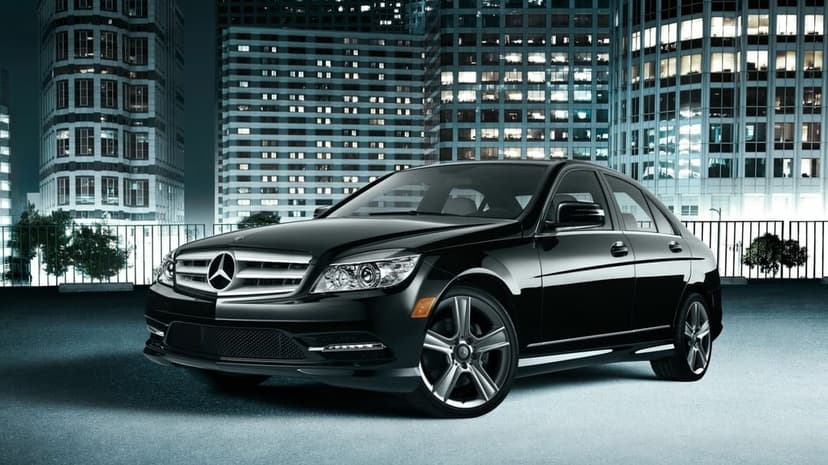 Glossy black Mercedes-Benz sedan parked in front of glowing skyscrapers at night with sharp urban lighting.
