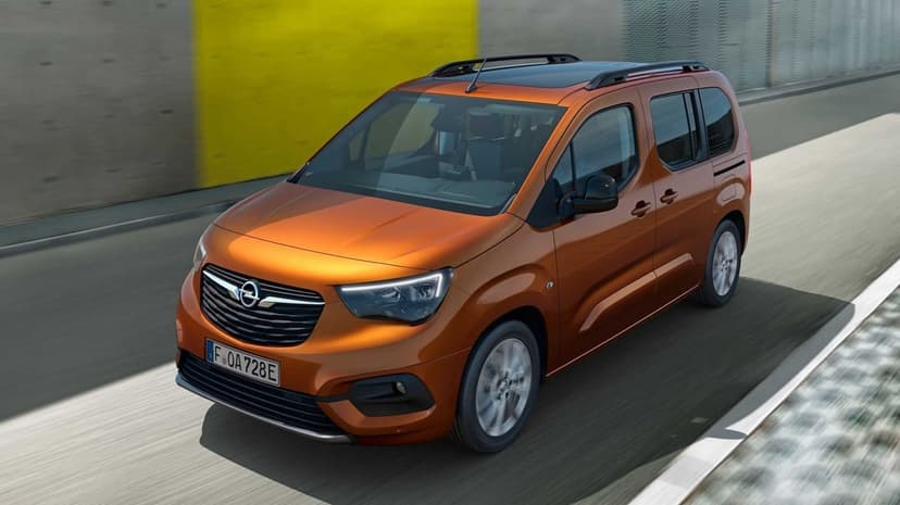 Orange Opel Combo-e Life electric car driving on a road past a yellow wall in bright daylight.