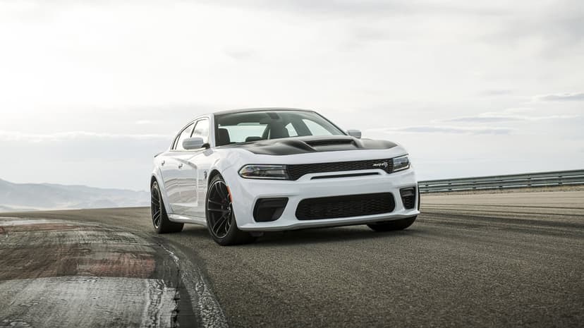 White Dodge Charger SRT Hellcat Widebody with black hood on an asphalt racetrack under an overcast sky.