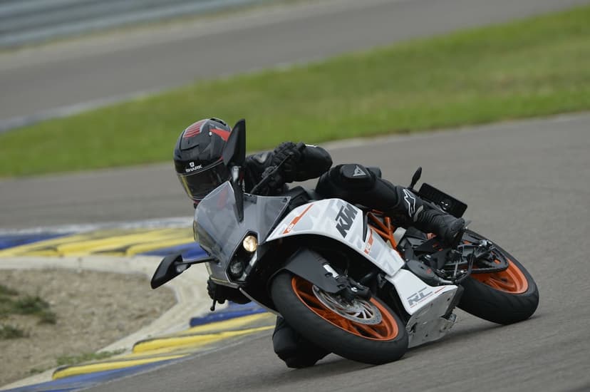 Professional motorcyclist leaning a KTM RC sportbike into a sharp turn on a paved racetrack circuit.