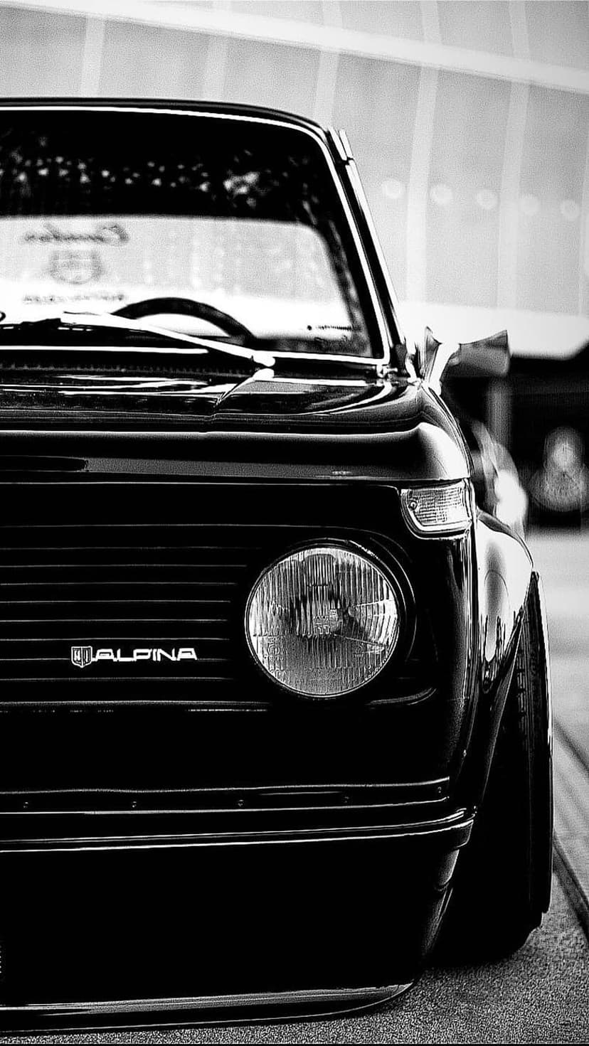 BMW Alpina circular headlight and vertical chrome grille slats shown in a monochrome close-up photography shot.