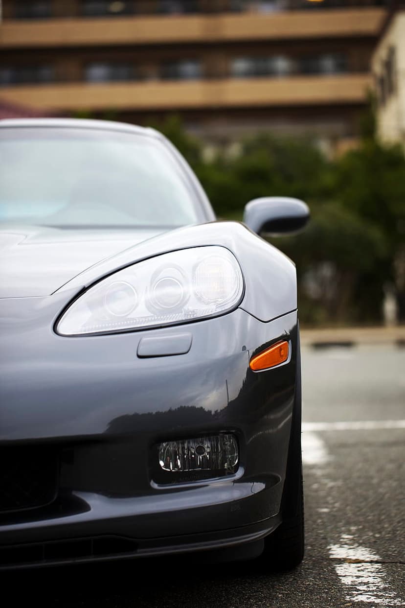 Dark gray sports car headlight with an orange turn signal and polished paint reflections in an outdoor setting.