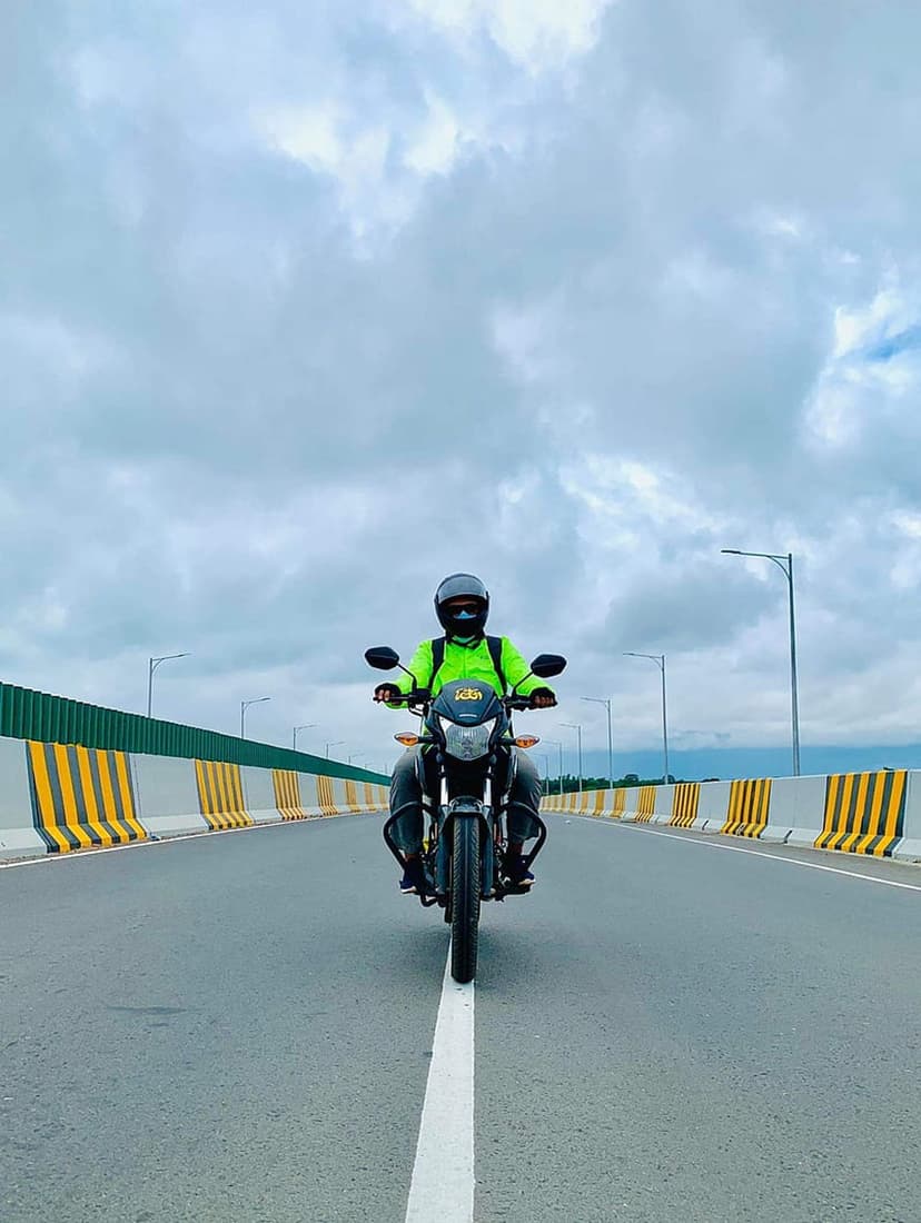 Motorcyclist in a neon green jacket riding on a highway under a dramatic cloudy sky with yellow road barriers.
