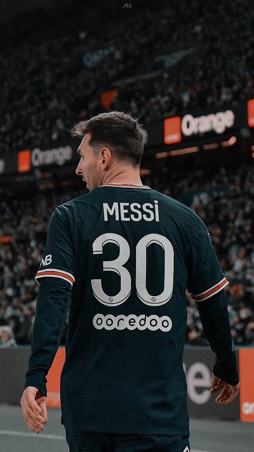 Lionel Messi in a navy PSG jersey with number 30 looks over his shoulder inside a brightly lit football stadium.