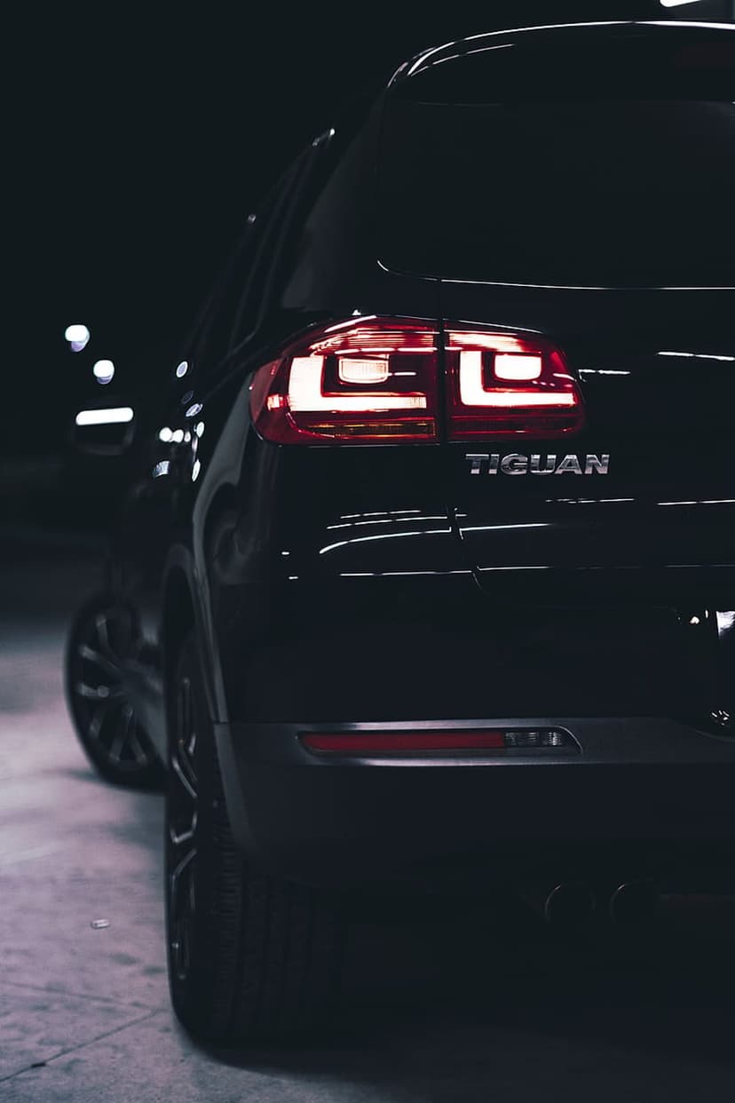 Volkswagen Tiguan rear LED tail lights glowing red against polished black paint in a dim night setting.