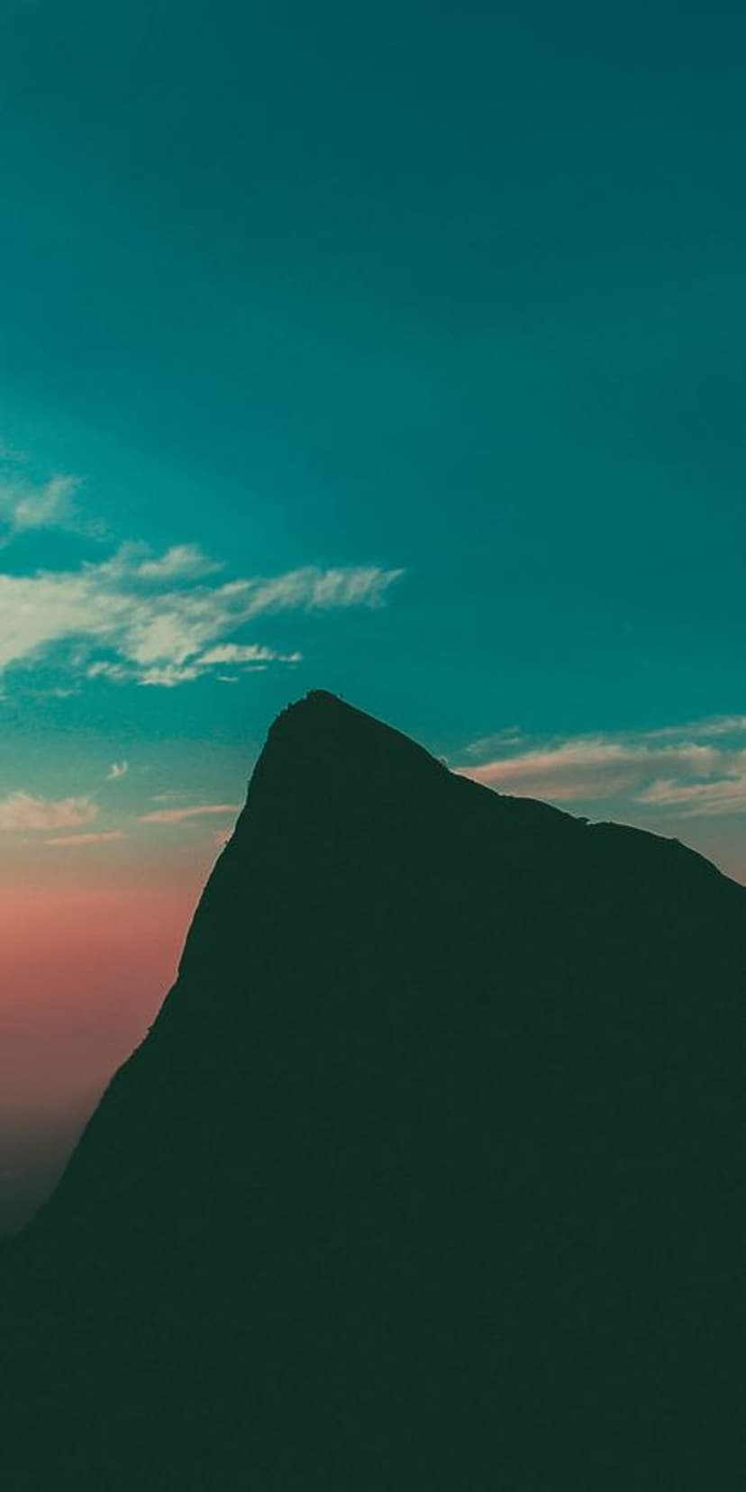 Sharp mountain peak silhouette against a turquoise and orange sunset sky with thin horizontal clouds.