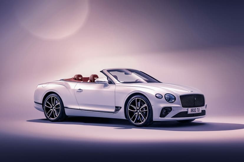 White Bentley Continental GT Convertible with red interior on a lavender studio background with soft lighting.