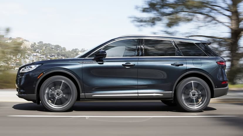 Side profile of a dark blue luxury SUV driving fast on a road with blurred background and spinning wheels.