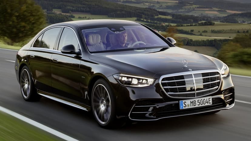 Black Mercedes-Benz S-Class luxury sedan driving on a scenic road with rolling hills in the background.