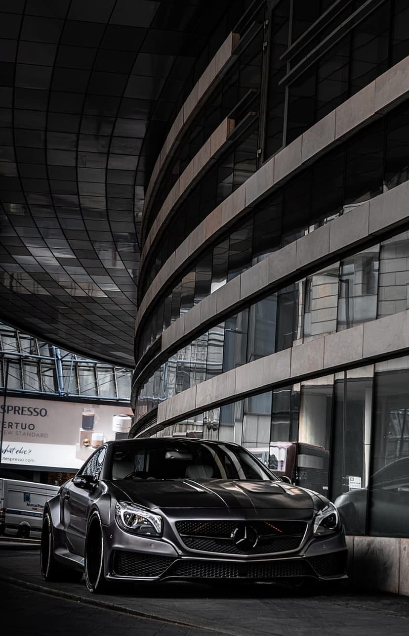Mercedes-Benz CLA coupe parked in front of a curved glass building with dark metallic reflections at night.