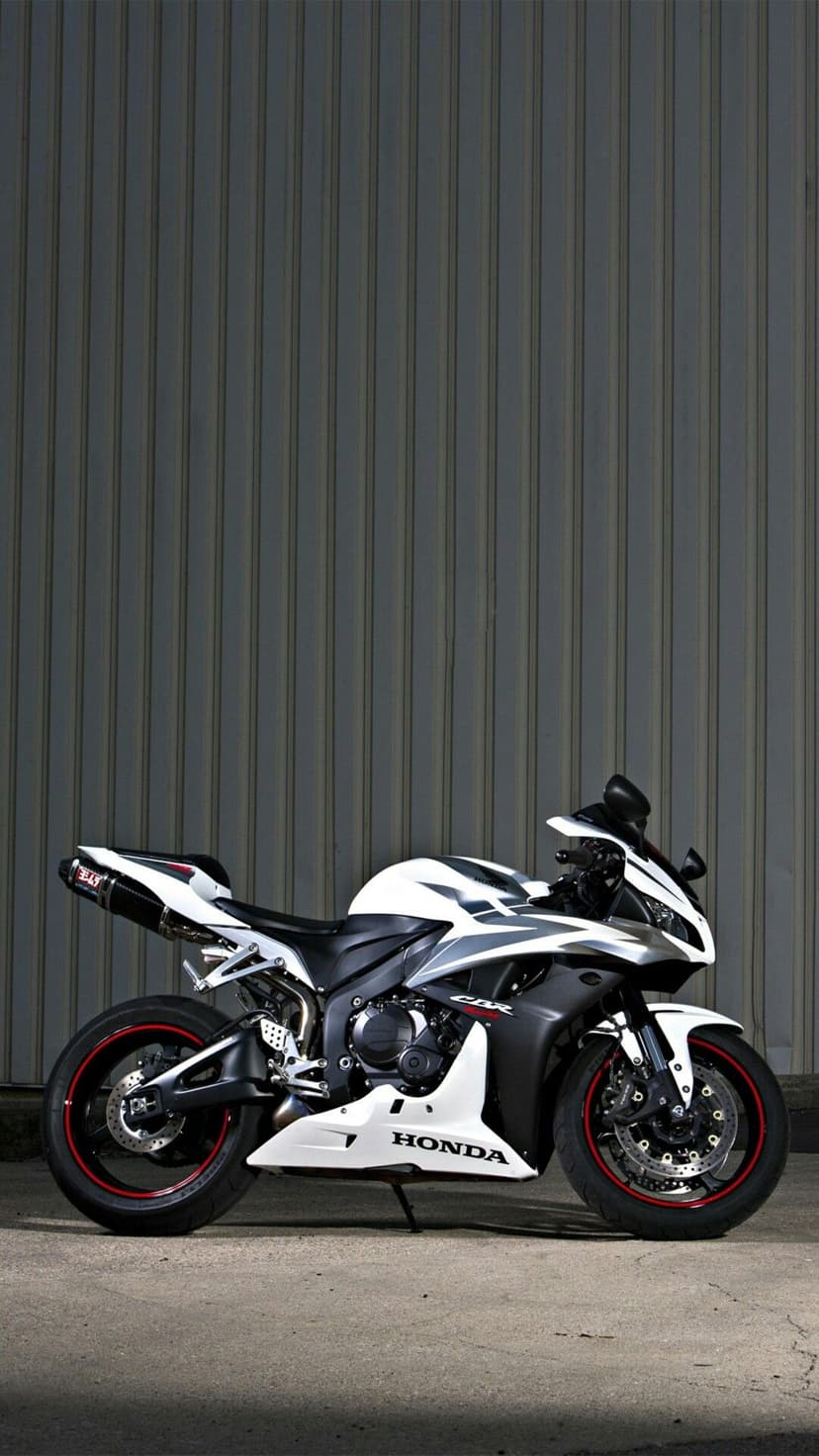 White Honda CBR motorcycle with red rim accents parked in front of a gray corrugated metal industrial wall.
