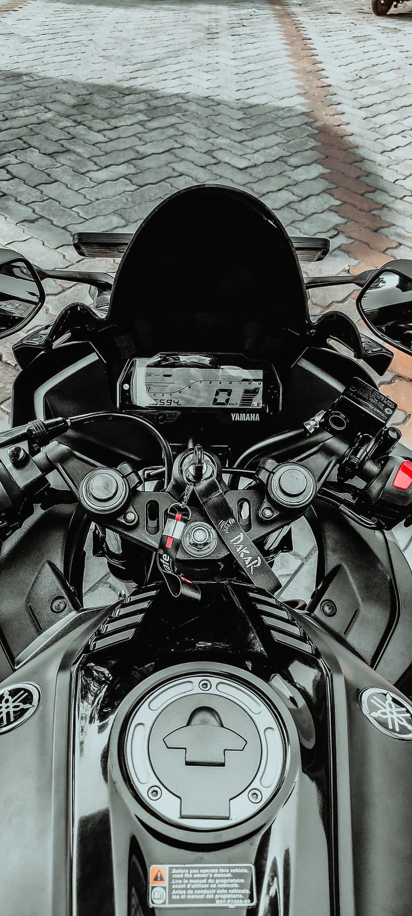 Yamaha R15 digital dashboard and fuel tank cap viewed from above, highlighting handlebars and a dakar keychain.
