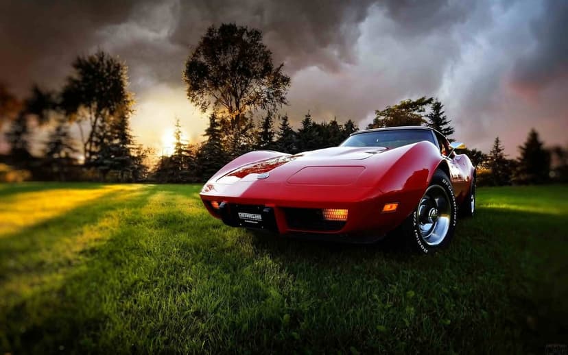 Red classic Corvette C3 on grass under dark storm clouds and golden sunlight for desktop background.
