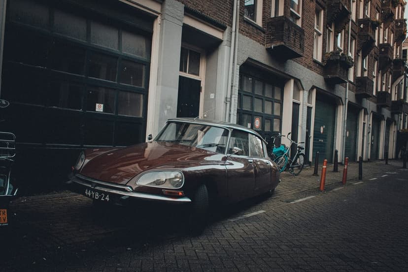 Burgundy Citroën DS parked on a narrow cobblestone street in front of historic European brick buildings and balconies.