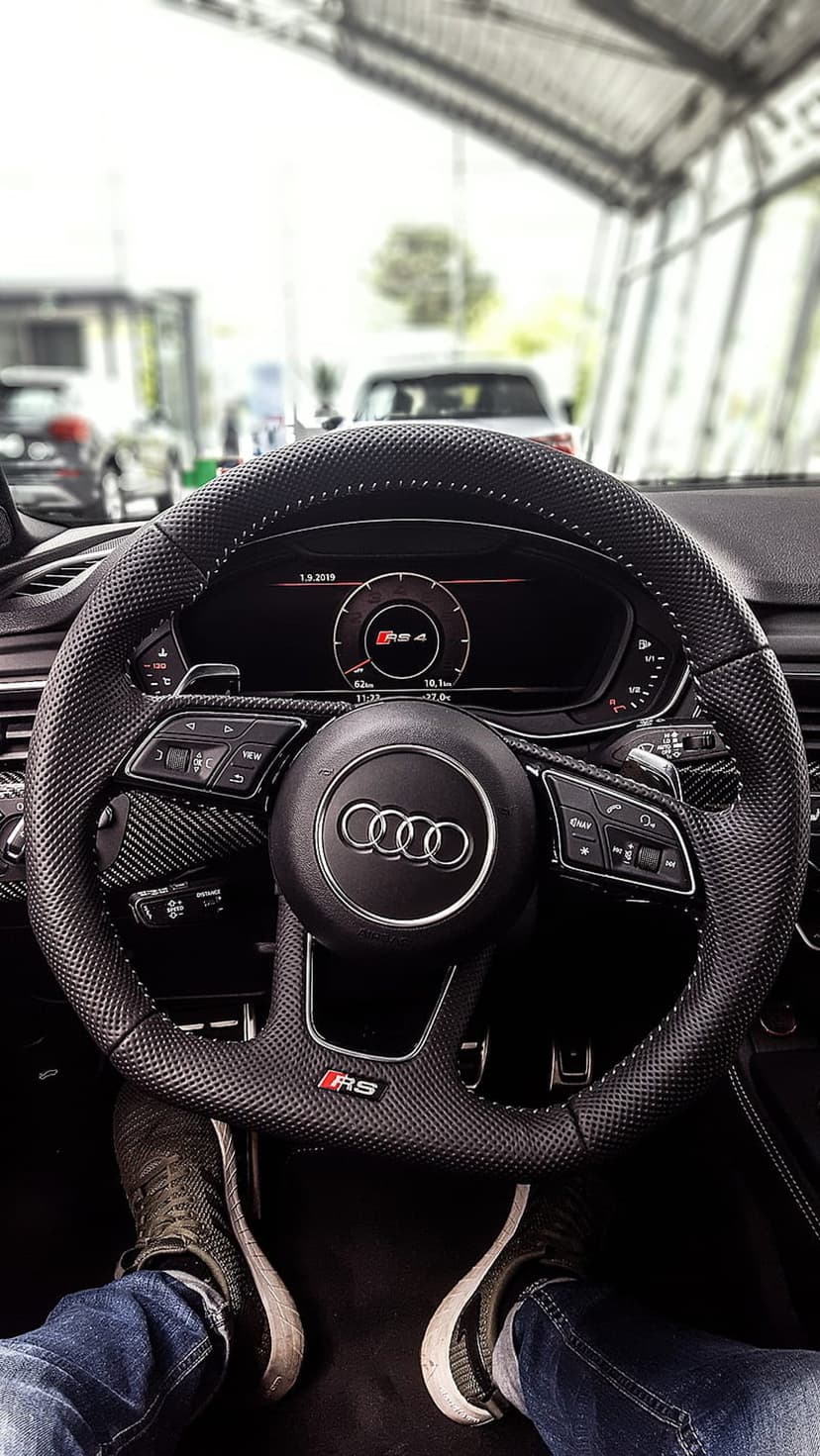 Audi RS4 steering wheel with carbon fiber accents and digital dashboard showing a red tachometer and RS4 logo.