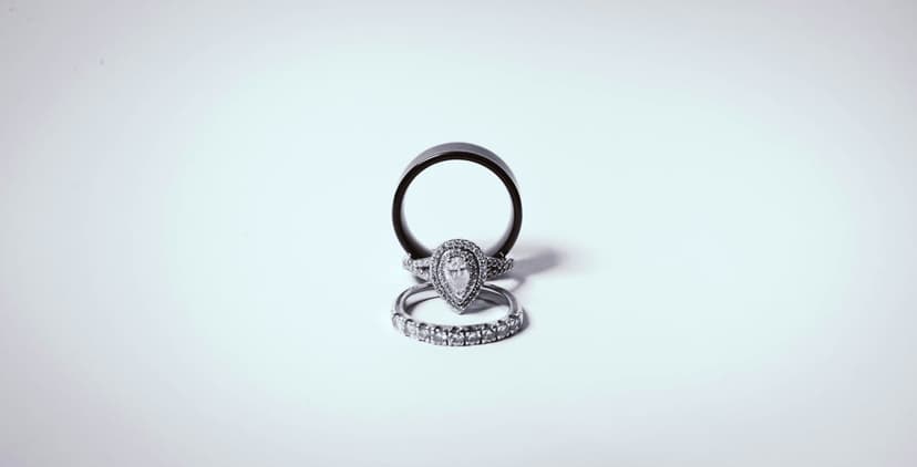 Pear-shaped diamond engagement ring and two wedding bands stacked together on a minimalist white background.