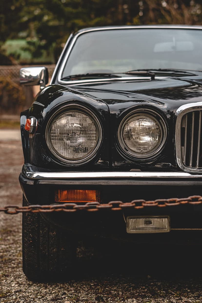 Black Jaguar XJ front end featuring dual round headlights, a chrome grille, and a rusty chain across the bumper.