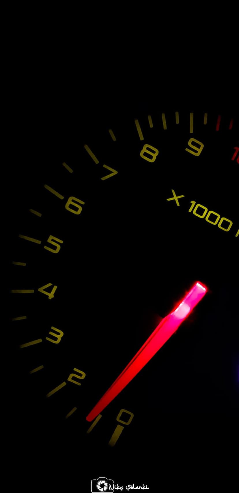Red tachometer needle points toward high RPMs on a yellow-scaled dashboard gauge against a black background.