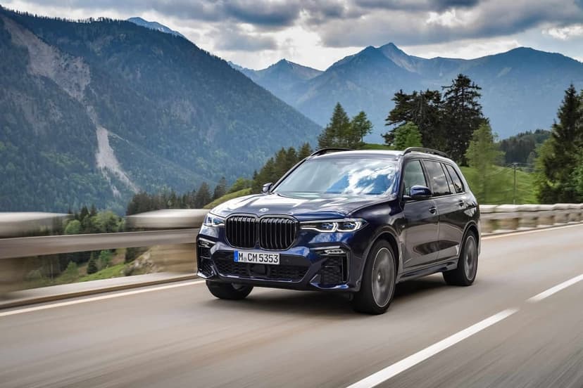 Dark blue luxury SUV driving on a mountain road with a backdrop of hazy peaks and green forests under a cloudy sky.