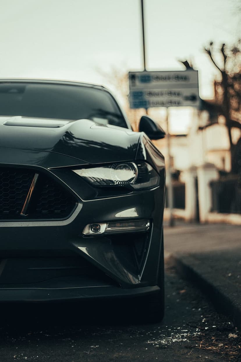 Ford Mustang headlight and black mesh grille shown in a low-angle close-up with a blurred street background.