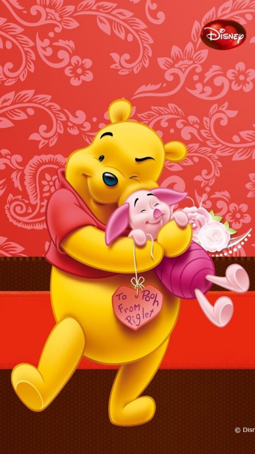 Pooh Bear hugs Piglet holding pink flowers and a heart tag against a red patterned floral background.