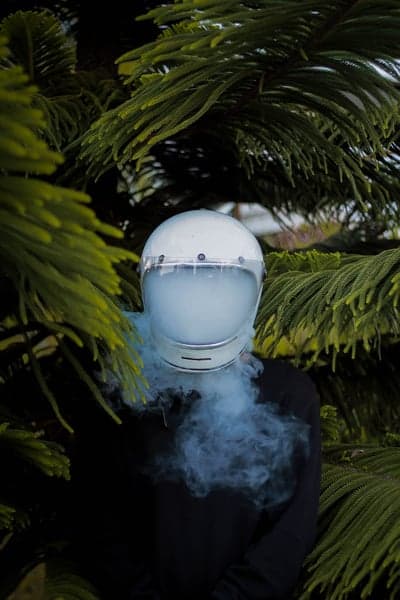Person in helmet exhaling smoke among pine trees