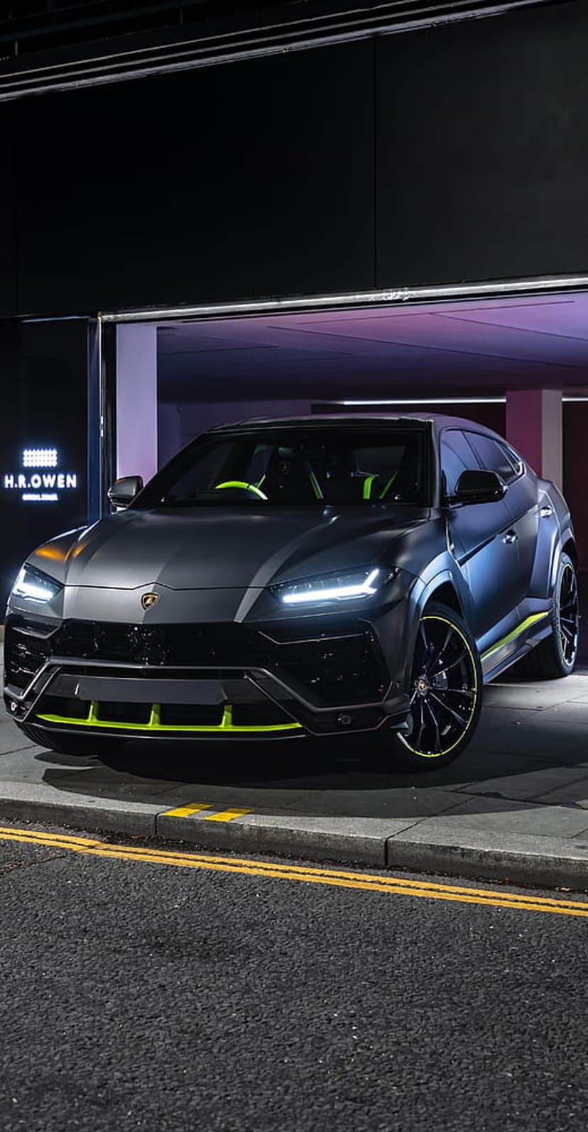 Lamborghini Urus in matte gray with neon green trims parked on a dark city street under midnight urban lighting.
