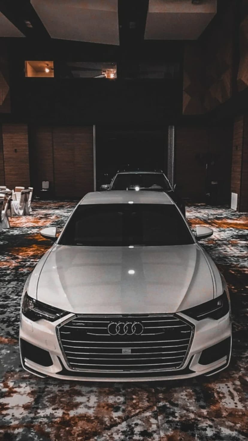 White Audi sedan front view with detailed honeycomb grille and headlights in a dimly lit indoor event space.