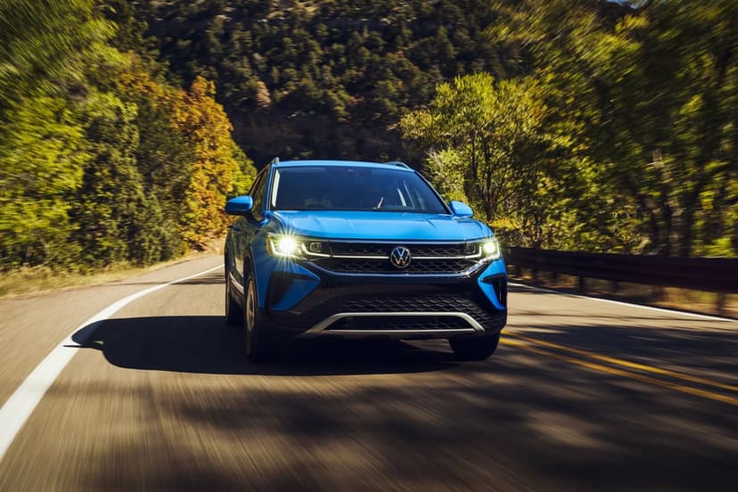 Blue Volkswagen SUV driving on a winding mountain road through a sunlit forest with dynamic motion blur effect.