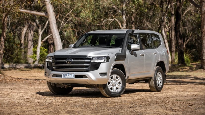 Silver Toyota Land Cruiser with a snorkel parked on a dirt path in a sunny forest with tall gum trees.