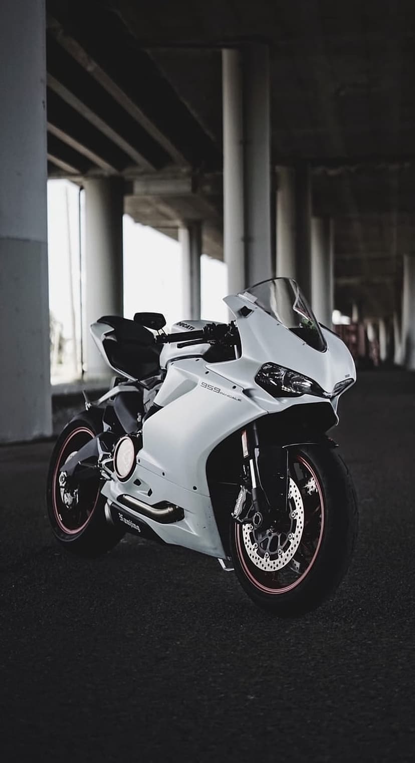 White Ducati Panigale motorcycle parked under a concrete bridge with industrial lighting and black accents.