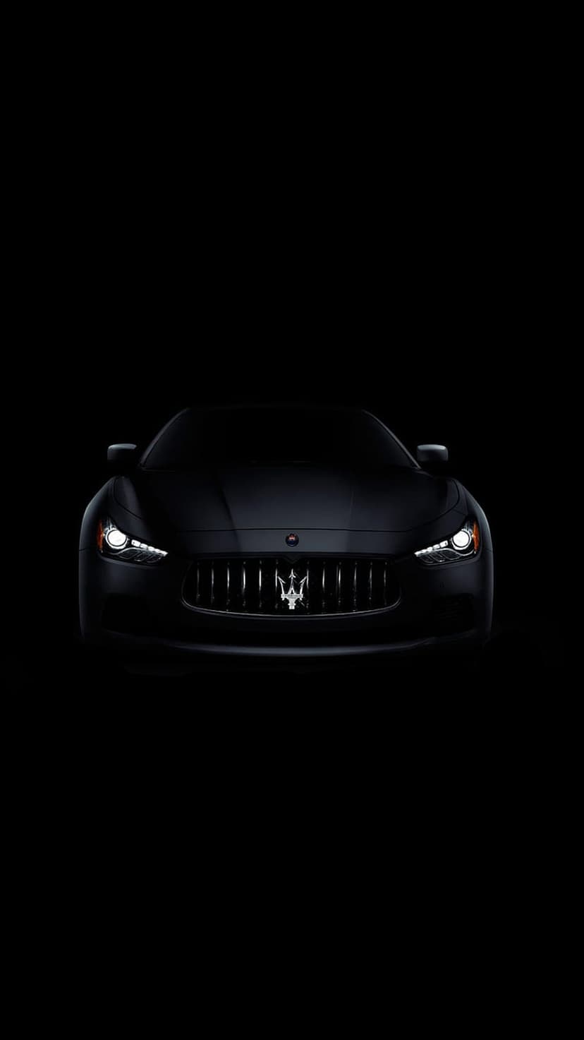 Maserati Ghibli front grille and glowing headlights emerge from a dark black background in sharp focus.