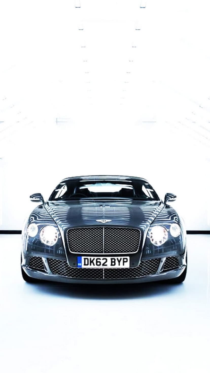 Bentley Continental GT front grille and glowing LED headlights in a grey studio setting for a phone background