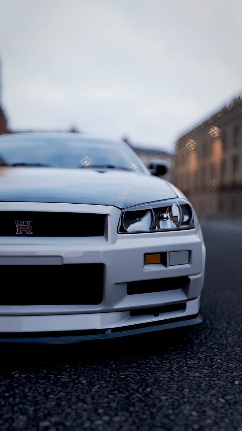 Nissan Skyline R34 front grille and aggressive headlights with a white paint finish against blurred city lights.
