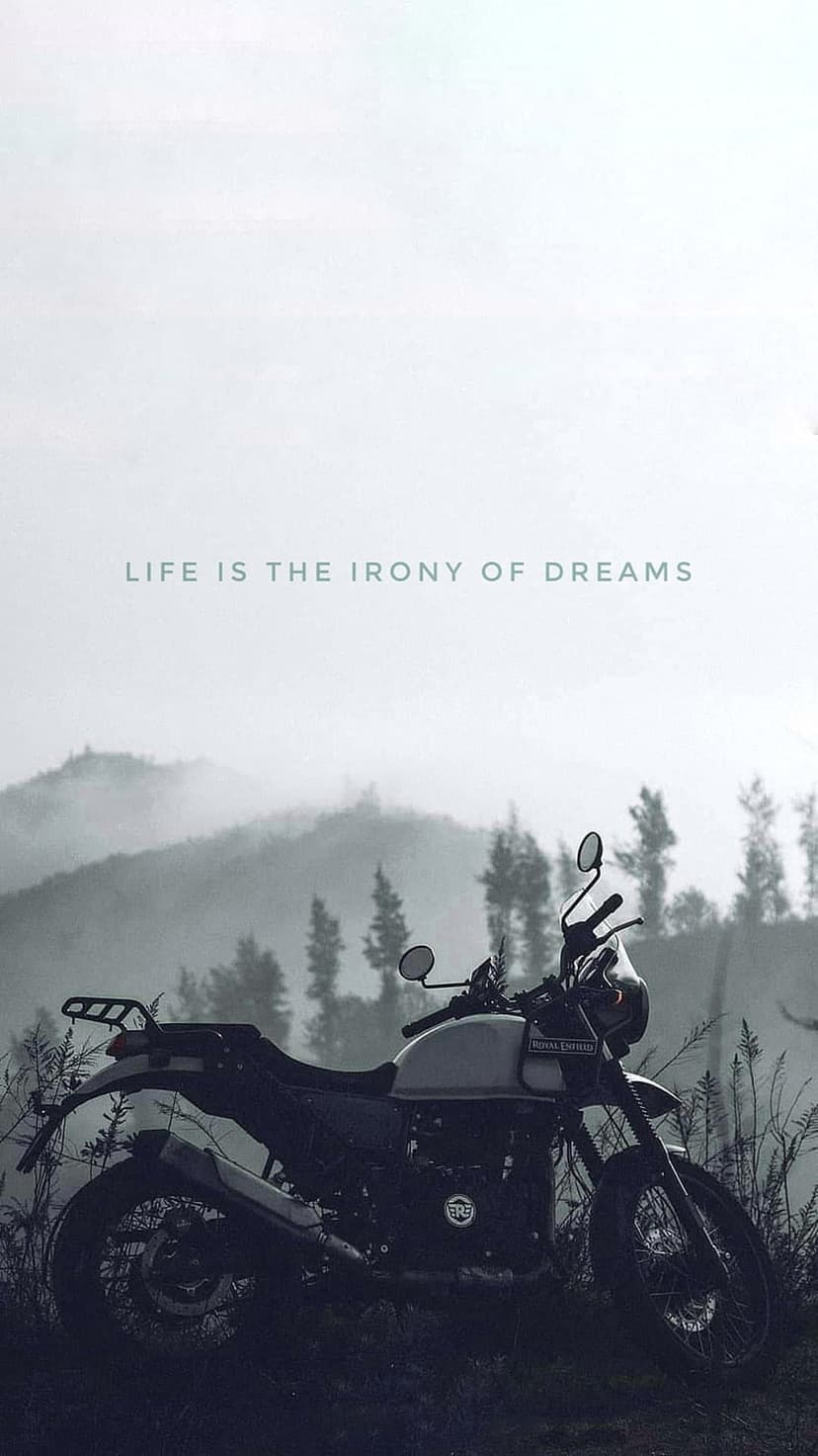 Vintage motorcycle parked on a rocky path overlooking fog-covered mountains with the text Life is the irony of dreams.
