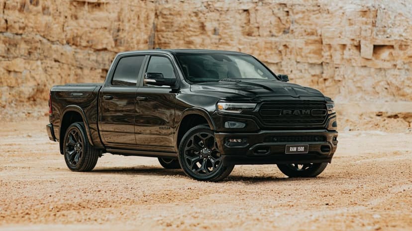 Black RAM 1500 pickup truck parked on sandy ground in front of a tall, textured limestone cliff face.
