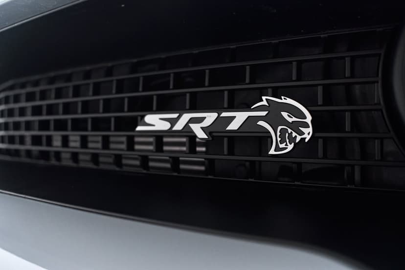 SRT Hellcat logo and white lettering centered on a black rectangular mesh car grille with soft lighting.