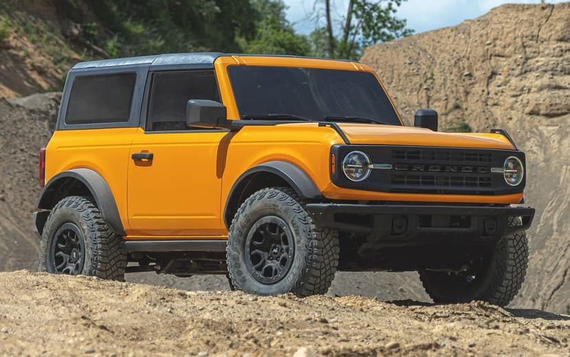 Yellow 2-door Ford Bronco with black accents parked on a dirt hill in a sunlit quarry under a clear sky.
