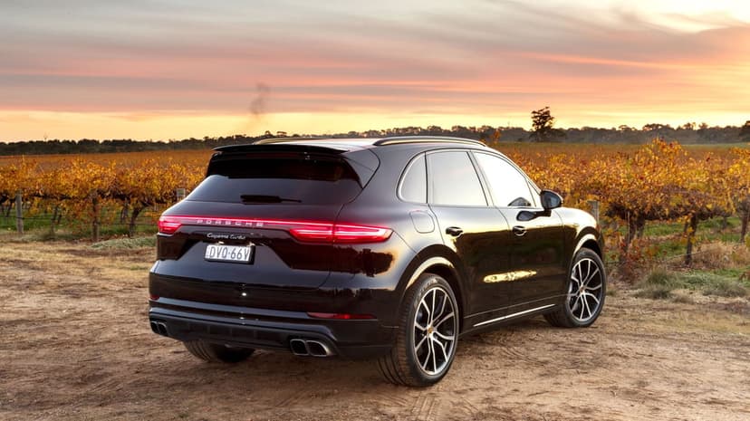 Black Porsche Cayenne Turbo parked in a sunset vineyard with glowing taillights and autumn leaves.