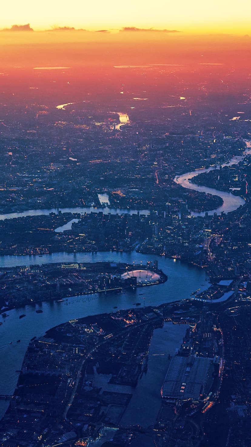 Thames River curves through a sprawling London cityscape illuminated by sunset light and golden evening street lamps.