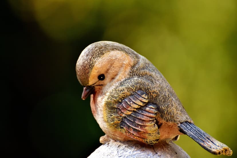 Small garden bird statue with an orange chest and grey feathers perched on a white surface with blurred background