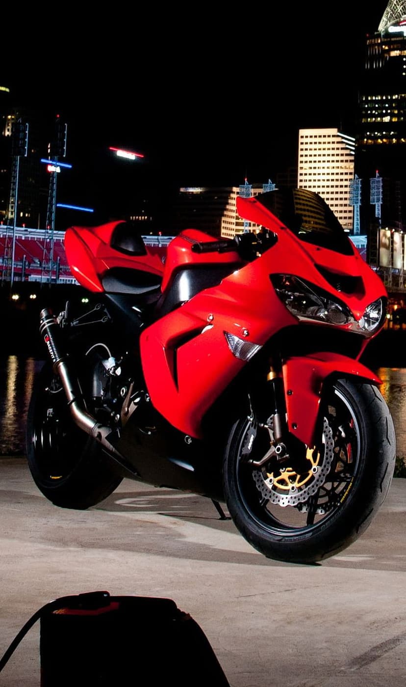 Red sport motorcycle parked on a dark urban street with a brightly lit metropolitan skyline in the background.