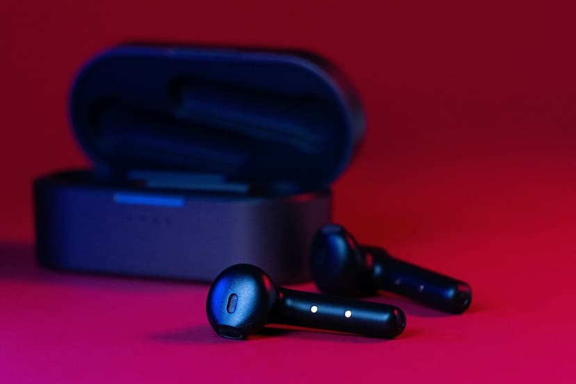 Black wireless earbuds in an open case illuminated by red and blue neon lights on a crimson background.