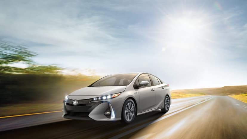 Silver Toyota Prius Prime hybrid driving fast on a sunlit road with heavy motion blur and a bright sun flare.